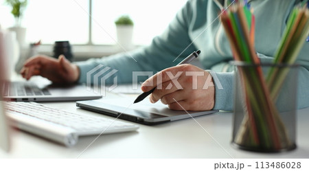 A young designer holds a pen from a tablet in his A young designer holds a pen from a tablet in his 113486028