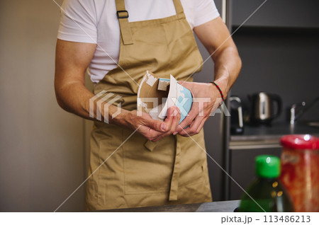 Close-up man chef in beige apron, pouring some salt from paper bag, seasoning meal while cooking dinner Close-up man chef in beige apron, pouring some salt from paper bag, seasoning meal while cooking dinner 113486213