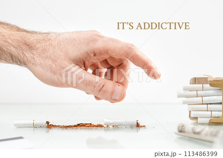 The concept of nicotine dependence and tobacco Smoking. On the surface lies a broken cigarette, a dollar bill, and a pack of cigarettes, to which a man's hand reaches.White background. It's addictive 113486399