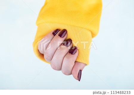 A woman's hand in a yellow jacket with a stylish blackberry-colored manicure. A woman's hand in a yellow jacket with a stylish blackberry-colored manicure. 113488233