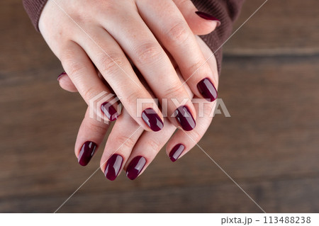 Female hands with blackberry-colored manicure over wooden background. Female hands with blackberry-colored manicure over wooden background. 113488238
