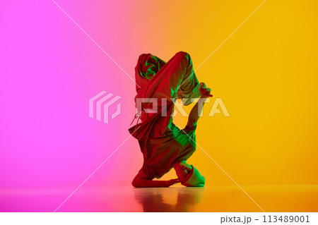 Creative, dynamic photo of breakdance performing freezes in neon light against gradient pink-yellow background. 113489001