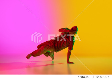 Cool attitude young man performing breakdance in motion in neon light against gradient pink-yellow background. 113489007