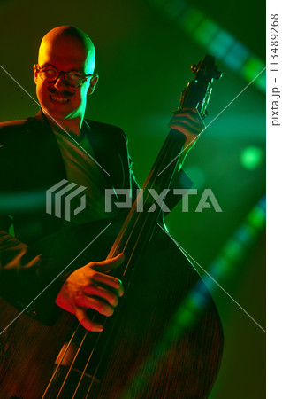 Contemporary double bass player in silhouette in red-green neon light against gradient studio background. 113489268