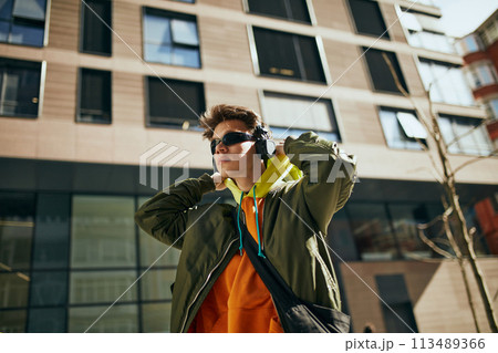 Cool attitude young guy, in overcited bright clothes, reflecting essence of modern street style against city landscapes. Cool attitude young guy, in overcited bright clothes, reflecting essence of modern street style against city landscapes. 113489366