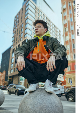 Young man poses against bustling cityscape, his neon over-size outfit bold statement of modern street fashion. 113489374