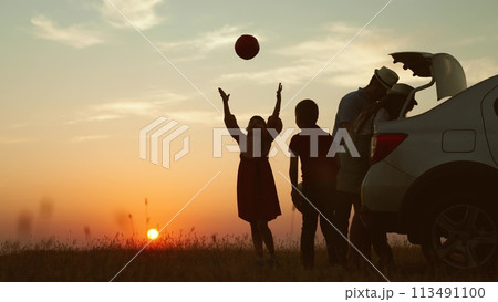 Playful family at sunset by car. cheerful children parents going on travel road trip by automobile packing baggage putting luggage in trunk kids playing ball. Packing preparation for family picnic. Playful family at sunset by car. cheerful children parents going on travel road trip by automobile packing baggage putting luggage in trunk kids playing ball. Packing preparation for family picnic. 113491100