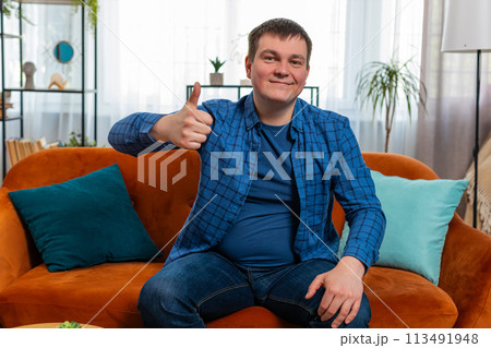 Excited Caucasian man looking approvingly at camera showing thumbs up like sign satisfied feedback 113491948