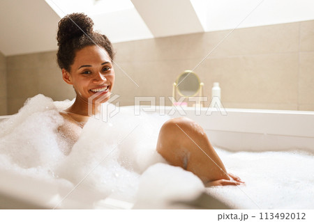 A woman smiles with comfort while bathing in a foamy bathtub A woman smiles with comfort while bathing in a foamy bathtub 113492012
