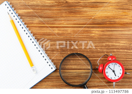 School notepad with alarm clock on wooden desk. 113497786