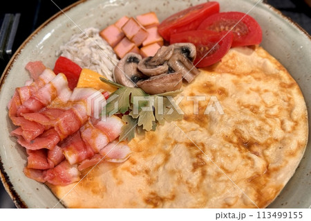 Scrambled eggs with bacon, mushrooms, tomatoes on a plate on a table. Close-up 113499155