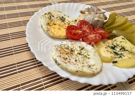 Round fried eggs with tomatoes on a white plate on a tablecloth. Close-up Round fried eggs with tomatoes on a white plate on a tablecloth. Close-up 113499157