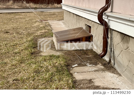 Brown stainless steel drain pipe for drain pipe with water drainage from roof the house to the ground. It attaches to a wall of residential building and leading to concrete surface 113499230