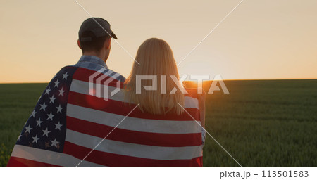 Two farmers with american flag on their shoulders looking forward in wheat field at sunset 113501583