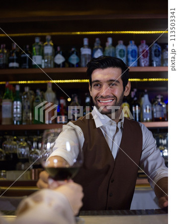 smiling bartender with classical metal shaker . Shelves with bottles of alcohol in background. smiling bartender with classical metal shaker . Shelves with bottles of alcohol in background. 113503341