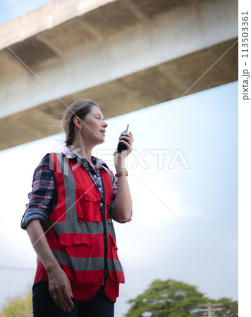 Woman railway engineer use walkie-talkie talking in to talk to maintenance department at site work of train garage. Woman railway engineer use walkie-talkie talking in to talk to maintenance department at site work of train garage. 113503361