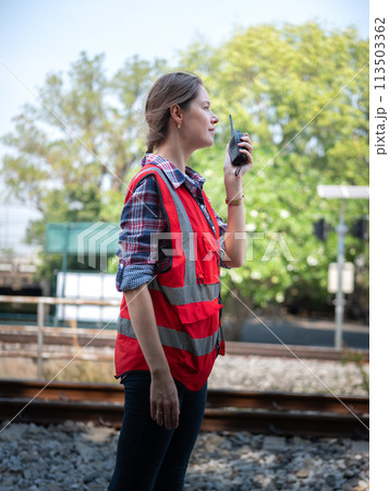 Woman railway engineer use walkie-talkie talking in to talk to maintenance department at site work of train garage. Woman railway engineer use walkie-talkie talking in to talk to maintenance department at site work of train garage. 113503362