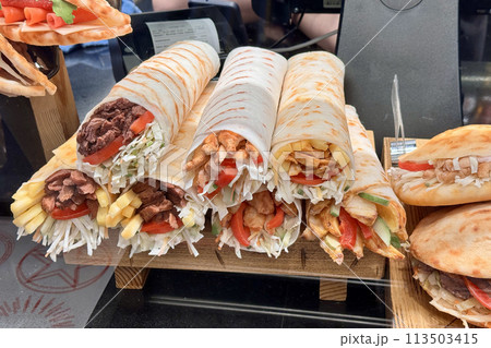 A variety of wraps and sandwiches made with fresh ingredients such as produce and vegetables are displayed on a wooden pallet. These fast food staples are perfect for a quick and delicious meal A variety of wraps and sandwiches made with fresh ingredients such as produce and vegetables are displayed on a wooden pallet. These fast food staples are perfect for a quick and delicious meal 113503415