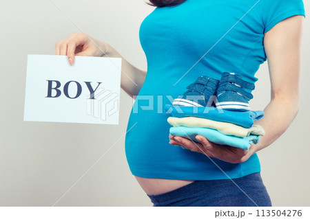 Woman in pregnant holding card with inscription boy and clothes for newborn 113504276