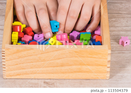 Hands of kid playing thread and colorful beads used to making bracelets 113504379