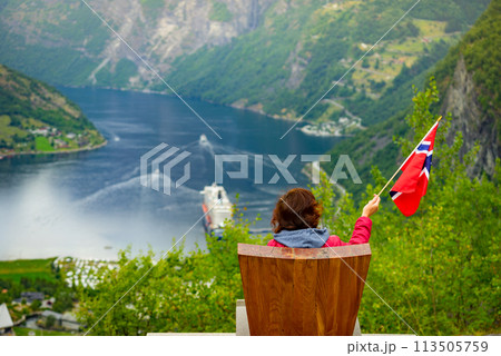 Tourist over Geirangerfjord holds norwegian flag Tourist over Geirangerfjord holds norwegian flag 113505759