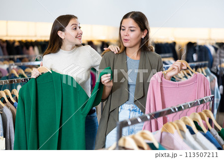 Two young women comparing green and pink cardigans while spending time together in a shopping mall Two young women comparing green and pink cardigans while spending time together in a shopping mall 113507211