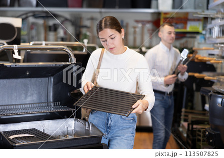 In store, girl inspects mobile grill, buys barbecue device 113507825