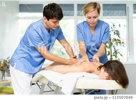 Young masseur trainee with female mentor doing back massage to woman Young masseur trainee with female mentor doing back massage to woman 113507849
