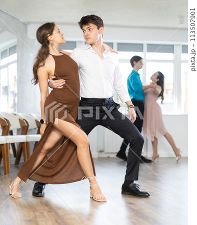 Girl and guy in festive clothes dancing slow ballroom dance during group lesson in choreography studio Girl and guy in festive clothes dancing slow ballroom dance during group lesson in choreography studio 113507901