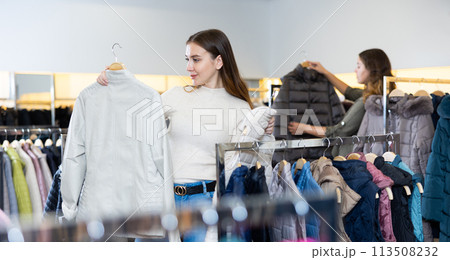 Young female consumer choosing windbreaker jackets in shopping center Young female consumer choosing windbreaker jackets in shopping center 113508232