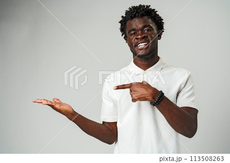 Young African Man Pointing at Something Against Gray Background Young African Man Pointing at Something Against Gray Background 113508263