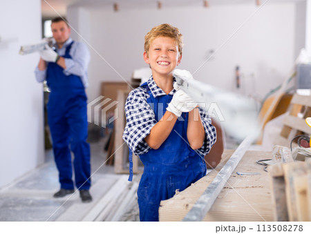 Boy carrying metal plank with his father in construction site Boy carrying metal plank with his father in construction site 113508278