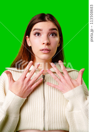 Young Woman With a Surprised Expression Standing Against a Green Background in Daylight 113508683