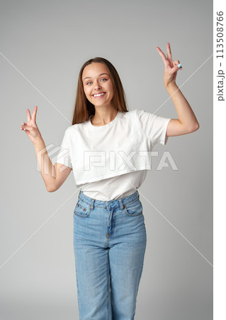 Smiling young woman showing victory sign on gray background Smiling young woman showing victory sign on gray background 113508766