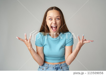 Happy cute young beautiful woman looking excited and surprised on gray background Happy cute young beautiful woman looking excited and surprised on gray background 113509056