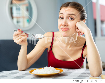 Young woman eating rice while sitting at the table in room. Diet and weight loss concept 113509113