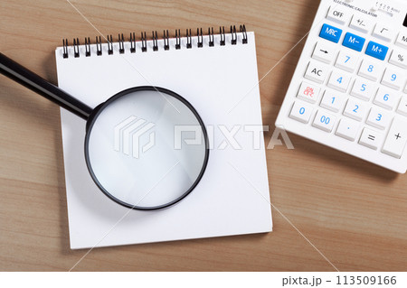 notebook on a brown wooden background with a calculator and magnifying glass 113509166