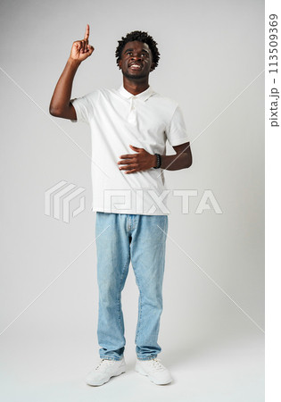 Young African Man in Casual Attire Pointing Upwards With a Smile Against a Grey Background Young African Man in Casual Attire Pointing Upwards With a Smile Against a Grey Background 113509369