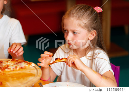 Young Girl Enjoying a Slice of Pizza at a Birthday Party Indoors 113509454
