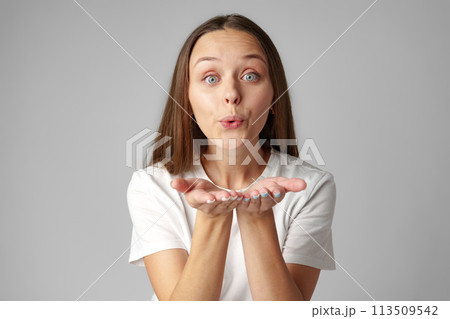 Young woman blowing a kiss to camera on gray background 113509542