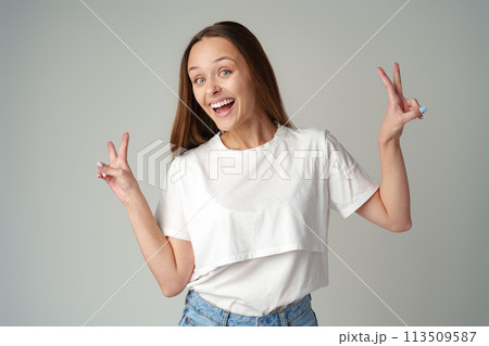 Smiling young woman showing victory sign on gray background 113509587