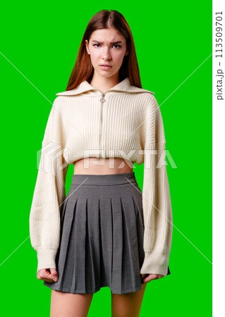 Young Woman Posing in Stylish Cropped Jacket and Pleated Skirt Against Green Background 113509701