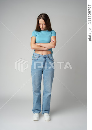Portrait of sad displeased offended young woman in blue T-shirt on gray background Portrait of sad displeased offended young woman in blue T-shirt on gray background 113509797