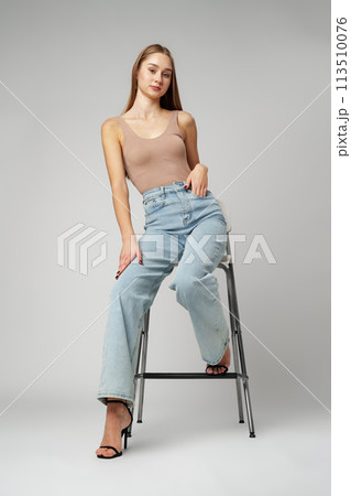 Young Woman Sitting on Stool in High Rise Jeans on gray background Young Woman Sitting on Stool in High Rise Jeans on gray background 113510076