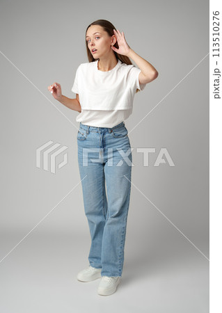 Young woman listening with her hand on an ear on gray background 113510276