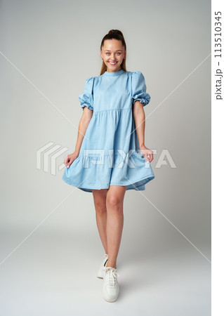 Young happy smiling woman in a light blue dress on a gray background 113510345