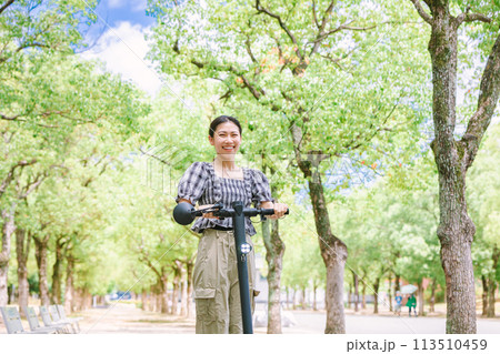 電動キックボードで並木道を走る若い女性 電動キックボードで並木道を走る若い女性 113510459