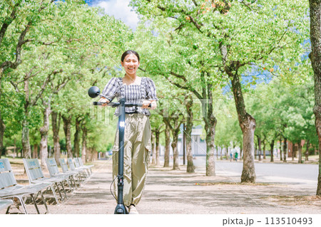 電動キックボードで並木道を走る若い女性 113510493