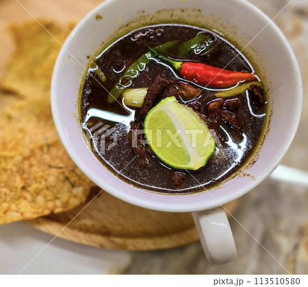 Rawon or Indonesian black beef soup, black color are from indonesian nut called kluwek. Served with lime, chili paste, salted egg, and tempe cracker. Perfect for recipe, article, or any cooking 113510580