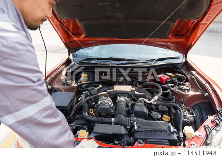 A mechanic in uniform and protective glove looks at a sport car's engine to fix it. Working atmosphere at car repair shop. A mechanic in uniform and protective glove looks at a sport car's engine to fix it. Working atmosphere at car repair shop. 113511948